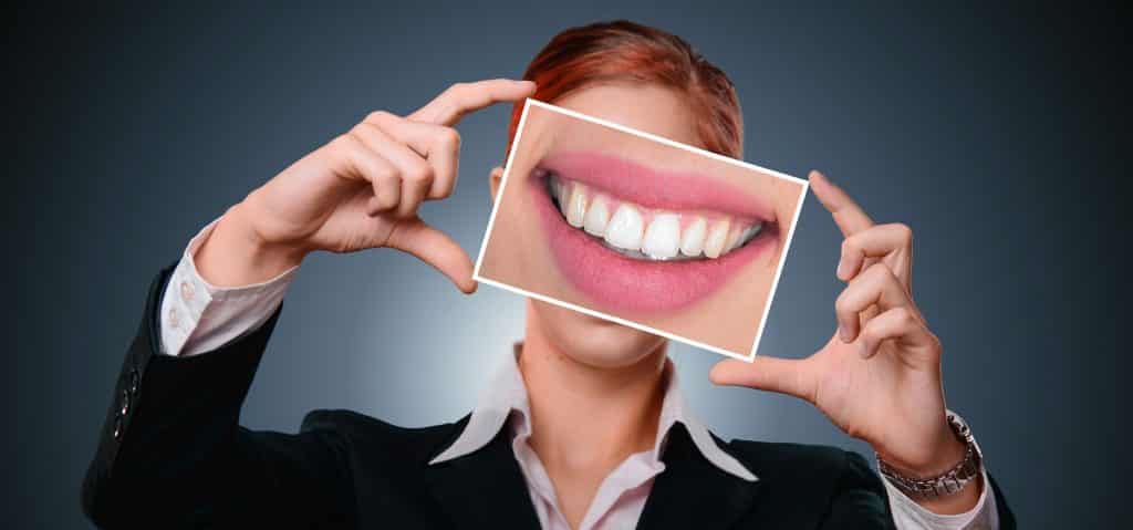 Hình ảnh một người phụ nữ đang giơ trước mặt một bức ảnh miệng đang cười và để lộ hàm răng trắng đẹp.