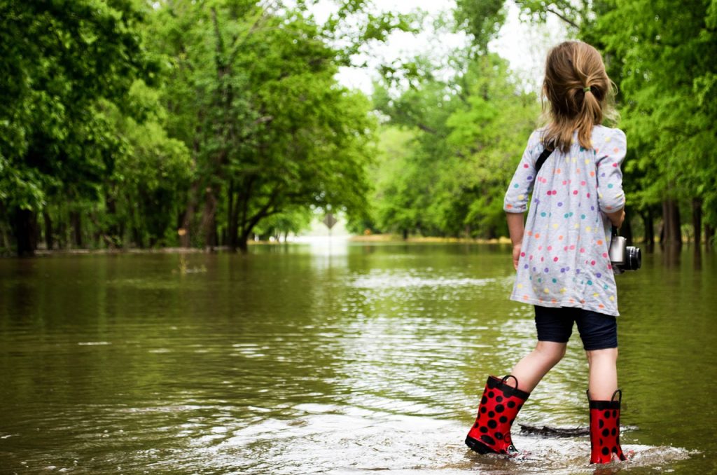 Cô gái trẻ với galoshes đi bộ trên sông lũ.